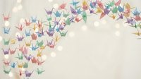 Colorful origami paper cranes flying across soft beige background with warm bokeh lights creating peaceful artistic composition for meditation and mindfulness designs.