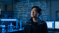 Young Asian male scientist or researcher standing in modern laboratory with mathematical equations and formulas projected on wall behind him in blue lighting.