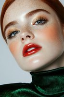 Close up beauty portrait of young woman with freckles, bright red glossy lips, natural makeup, blue eyes and ginger hair wearing emerald turtleneck.