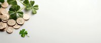 Lucky green clover leaves with golden coins scattered on white background. St Patrick's Day concept with copy space for seasonal promotions.