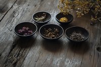 Assorted dried herbs and flowers in black ceramic bowls on rustic wooden table, moody lighting creates atmospheric composition for wellness and natural medicine.