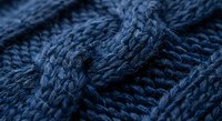 Close-up of navy blue cable knit wool texture showing intricate braided pattern and soft fibers for cozy winter fashion and textile design projects.