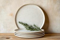 Stack of handmade ceramic plates with natural rim and rosemary sprig on wooden shelf against neutral background for kitchen and dining decor.