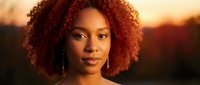 Young African American woman with curly red hair and earrings during golden hour sunset, warm lighting portrait for lifestyle and beauty content.