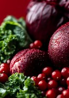 Fresh red plums with water drops and bright cranberries on dark background with green kale leaves, macro food photography for healthy eating concept.