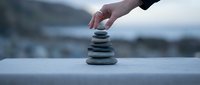 Hand placing smooth stone onto balanced stack, symbolizing harmony, mindfulness, and equilibrium for wellness and meditation concepts.