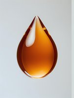 Amber-colored liquid drop suspended in mid-air against light background, showcasing translucent honey-like substance with glossy surface and natural light reflection.