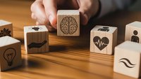 Hand holding wooden cube with brain icon among health and wellness symbol blocks on wood surface for medical education and mental health awareness.