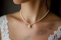 Elegant pearl pendant necklace on delicate silver chain against bride's neckline with white lace detail, showcasing minimalist bridal jewelry styling.
