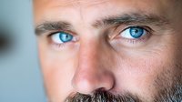 Close-up portrait of a Caucasian man with striking blue eyes, facial stubble, and intense gaze against soft background. Perfect for psychology or vision concepts.