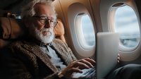 Senior businessman with glasses working on laptop during flight in airplane cabin for business travel and remote work productivity.