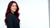 Professional young woman with long burgundy hair in dark blazer smiling confidently against white background for business and corporate presentations.