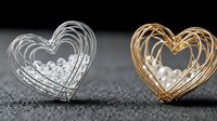 Two elegant wire heart-shaped jewelry pieces with pearls inside, silver and gold metal finish on dark textured surface for luxury accessories design.