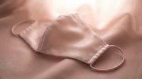 Pink silk face mask resting on soft fabric, elegant protective accessory in pastel rose tone, health and fashion concept.