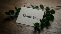 Thank you card on rustic wooden table with green eucalyptus leaves, elegant gratitude note for weddings, events, and personal messages.