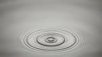 Water ripples creating concentric circles on calm surface with soft gray background for meditation and wellness concepts.