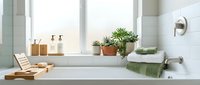 Modern minimalist bathroom with white bathtub, natural wood accessories, green plants and towels creating spa-like atmosphere for relaxation and wellness.