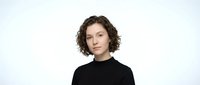 Young Caucasian woman with curly brown hair wearing black turtleneck sweater against white background. Professional portrait for business and lifestyle concepts.