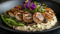 Grilled sea scallops with creamy risotto, sauteed asparagus and mushrooms on black plate garnished with purple edible flowers and microgreens.