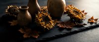 Autumn harvest display with dried sunflowers, ceramic pottery and fallen leaves on dark slate surface for seasonal home decor and thanksgiving styling.