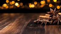 Star anise and cinnamon sticks on rustic wooden table with golden bokeh lights in background creating warm festive atmosphere for holiday season.