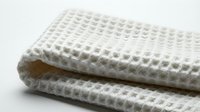 Folded white waffle weave cotton towel on light background, showcasing soft texture and clean minimalist style for home and spa concepts.