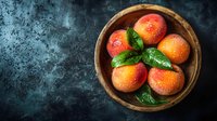 Fresh ripe peaches with water drops and green leaves in rustic wooden bowl on dark textured background, top view. Natural organic summer fruit.
