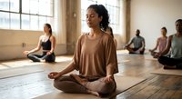Young African American woman practicing meditation in peaceful yoga studio with diverse group sitting cross-legged on wooden floor in natural sunlight.
