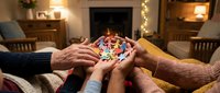 Group of people stacking hands together holding colorful puzzle piece in cozy living room with fireplace and warm lighting, symbolizing teamwork, unity, collaboration and problem solving.