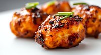 Grilled chicken meatballs glazed with sweet and spicy Asian sauce, garnished with fresh green onions on white plate, close up view with selective focus.