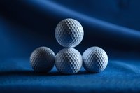 White golf balls arranged in triangle formation on blue textured surface with dramatic lighting and shadows creating professional sports composition.