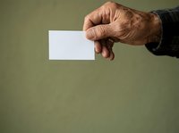 Senior man with wrinkled skin holding blank white business card or paper against green background for corporate branding and contact information display.