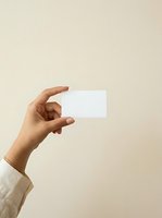 Hand holding blank white business card against neutral beige background, ideal for branding, corporate identity, and marketing mockup designs.