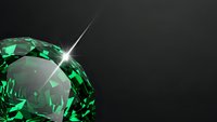 Brilliant green emerald gemstone with sparkling light reflection on dark background for luxury jewelry and precious stone designs.