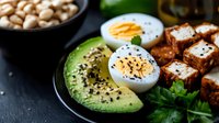 Healthy protein-rich meal with sliced avocado, hard-boiled eggs, seasoned tofu cubes and chickpeas on dark slate background for nutritious diet plans.