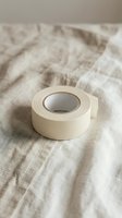 Roll of beige masking tape on wrinkled linen fabric background. Neutral tones adhesive tape for crafting, painting, packaging and DIY projects.