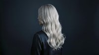 Young woman with long platinum blonde wavy hair wearing black leather jacket, rear view against dark background. Suitable for fashion, beauty, and lifestyle design projects.