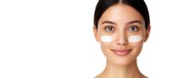 Young woman with under-eye patches and natural makeup smiling against white background, showcasing skincare and beauty treatment for cosmetic advertising.