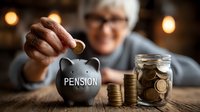 Senior woman with gray hair and glasses saving money in black piggy bank labeled pension, with stacked coins and jar on wooden table in warm lighting.