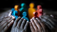 Colorful wooden figures standing together on diverse hands showing unity, support, and teamwork concept against dark background. Social inclusion metaphor.