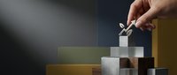 Hand placing final stone block on stacked tower of mixed materials, symbolizing business growth, achievement, and strategic planning for corporate success.