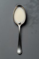 Silver spoon filled with fresh milk or cream on gray background for cooking, baking and dairy product concepts.