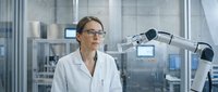 Female scientist with brown hair and glasses wearing white lab coat conducting research with robotic microscope equipment in modern laboratory setting for scientific research and technology concepts.