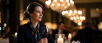Elegant middle-aged Caucasian businesswoman enjoying wine at upscale restaurant with warm chandelier lighting and sophisticated dining atmosphere.