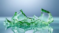 Shattered green glass pieces scattered on reflective surface with dramatic lighting and soft blue background, creating abstract artistic composition.