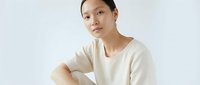Young Asian woman wearing cream-colored casual t-shirt, sitting with thoughtful expression against white background, suitable for lifestyle and wellness content.