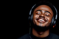 Happy young African American man enjoying music with headphones, smiling with eyes closed against black background for entertainment and lifestyle content.