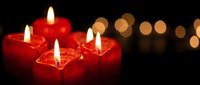 Red candles burning with warm flames creating cozy atmosphere against dark background with golden bokeh lights for romantic dinner or relaxation.