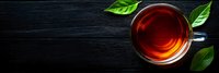 Glass cup of aromatic black tea with fresh green leaves on dark wooden background, top view panoramic shot with copy space for text.