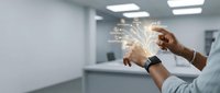Young male professional with dark skin tone wearing light blue shirt and smartwatch, holding glowing digital network visualization with light particles and connecting lines in modern office environment, representing technology innovation, data connectivity, and business solutions.